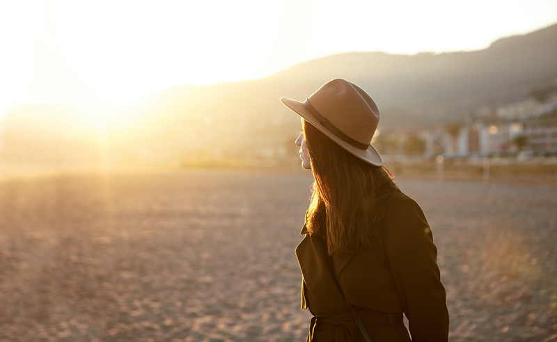 Eine Frau mit Hut genießt am Strand den Sonnenuntergang.