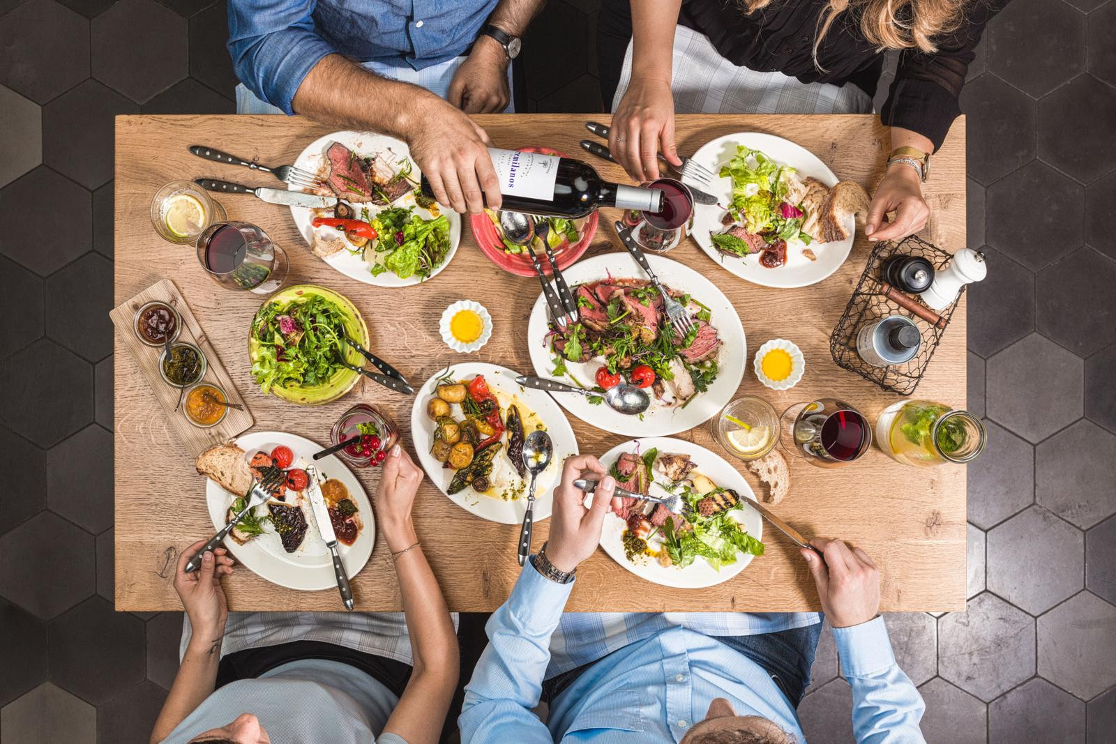 Blick von auf einen mit Speisen und Getränken gedeckten Tisch an dem vier Personen sitzen.