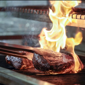 Auf dem offenen Flammengrill werden Fleischstücke gewendet.