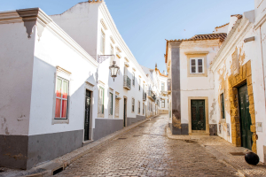 Blick in eine Kopfsteinpflastergasse in Faro, umsäumt von weißgetünchten Häusern.