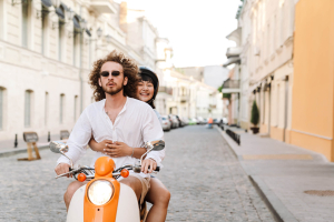 Junges Paar fährt auf einem Motorroller durch die sommerliche Straßen Roms.