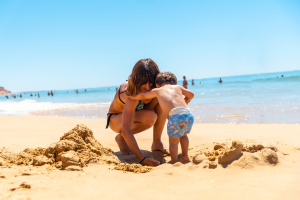 Junge Frau spielt mit kleinem Kind am Algarve-Strand.