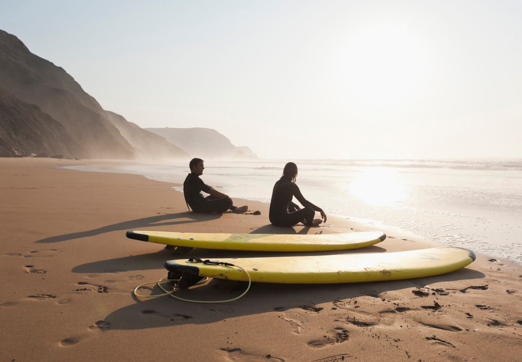 Abendstimmung: Junges Paar sitzt am Algarve-Strand. Neben ihnen liegen zwei Surfbretter.