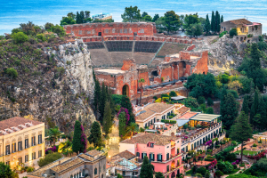 Blick auf das antike Theater in Taormina. Im vorderen Bereich ein Gebäudekomplex mit bunten Häusern in Terrassengärten.