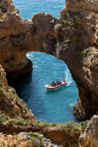 Vogelperspektive auf ein Touristenboot, das durch eine Algarve-Grotte gelenkt wird.