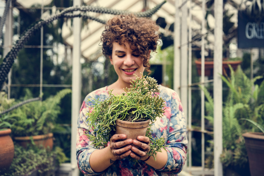 Eine Frau hält einen Topf mit einer Grünpflanze in ihren Händen.