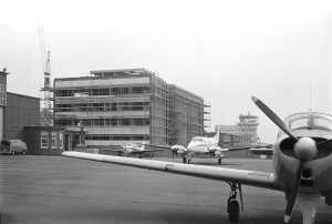 Bau der Radarkontrollzentrale Bremen in den 70ern. Vorne befinden sich Kleinflugzeuge und hinten steht der Rohbau und ein Kran.