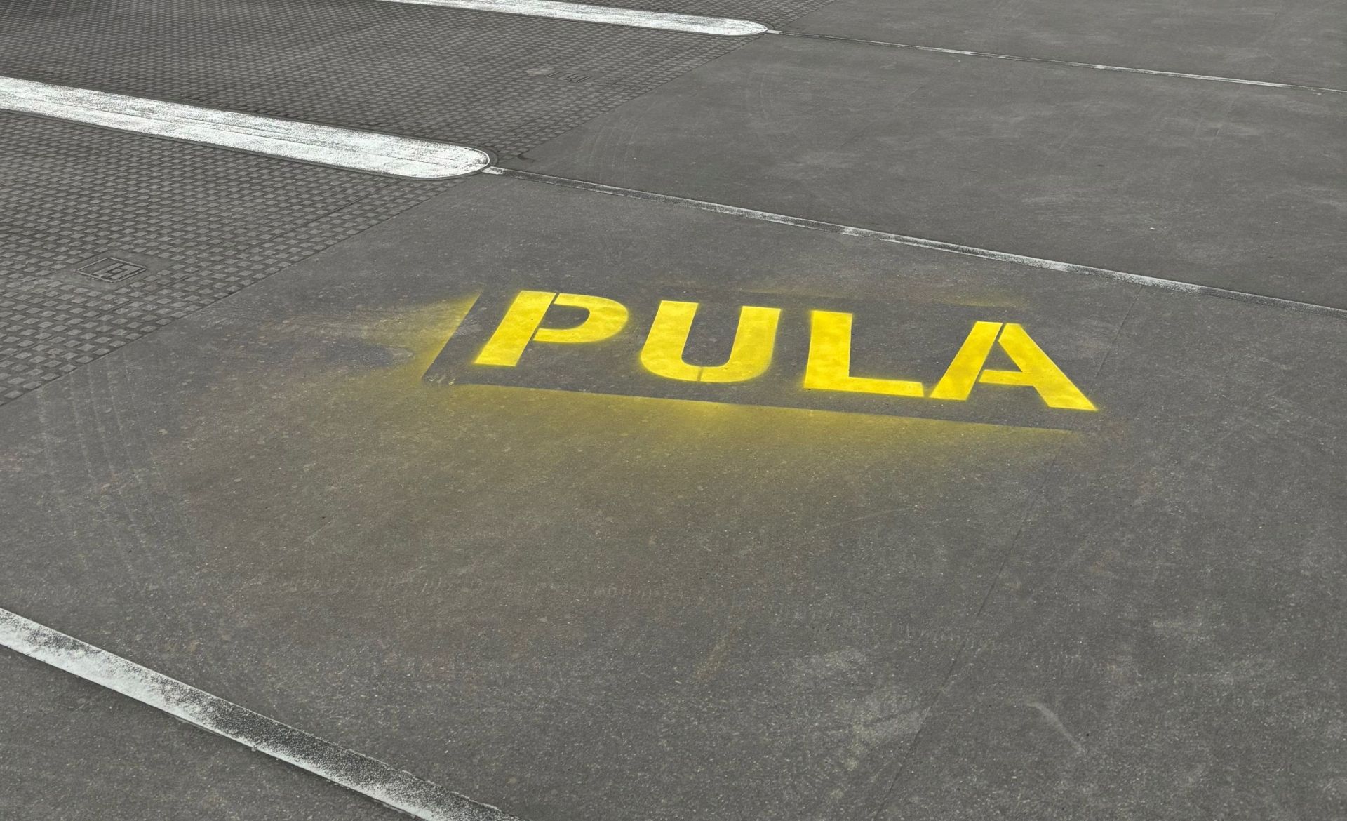 Auf dem gepflasterten Boden eines Parkhauses ist der Schriftzug Pula mit Kreidesprühfarbe zu lesen