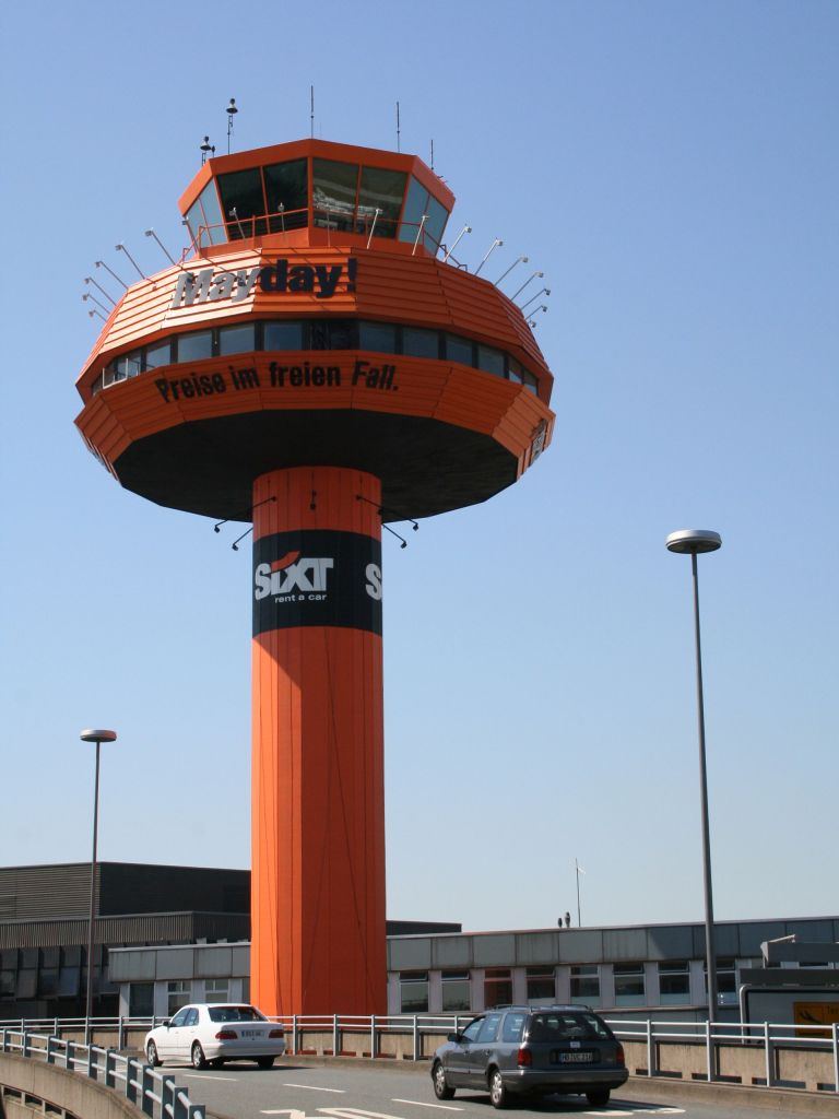 Der Tower mit der Werbung des Autovermieters SIXT s in den Farben Orange und Schwarz. Mit dem Schriftzug Mayday!