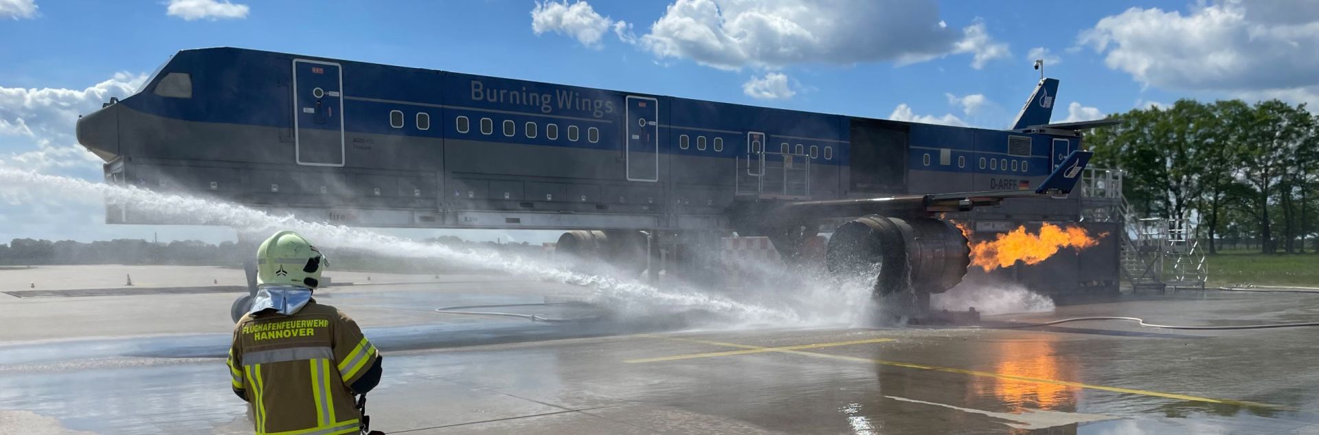 Ein Feuerwehrkollege beobachtet einen Triebwerksbrand an der Brandsimulationsanlage und den Angriff darauf.