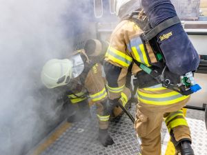 Zwei Kollegen der Flughafenfeuerwehr versuchen die Tür des Flugzeuges zu öffnen, aus der Rauch heraustritt