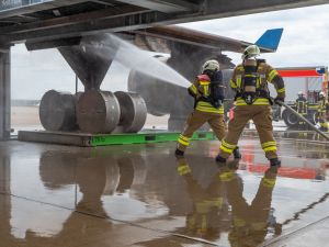 Zwei Kollegen der Flughafenfeuerwehr löschen einen Fahrwerkbrand an der Brandsimulationsanlage.