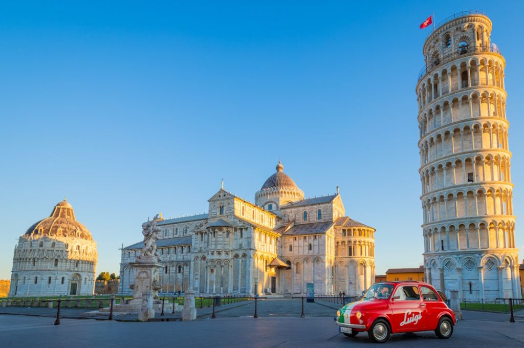 Vor dem schiefen Turm von Pisa steht ein kleiner Fiat 500 . Lackiert ist das Auto in den italienischen Landesfarben grün, weiß und rot.