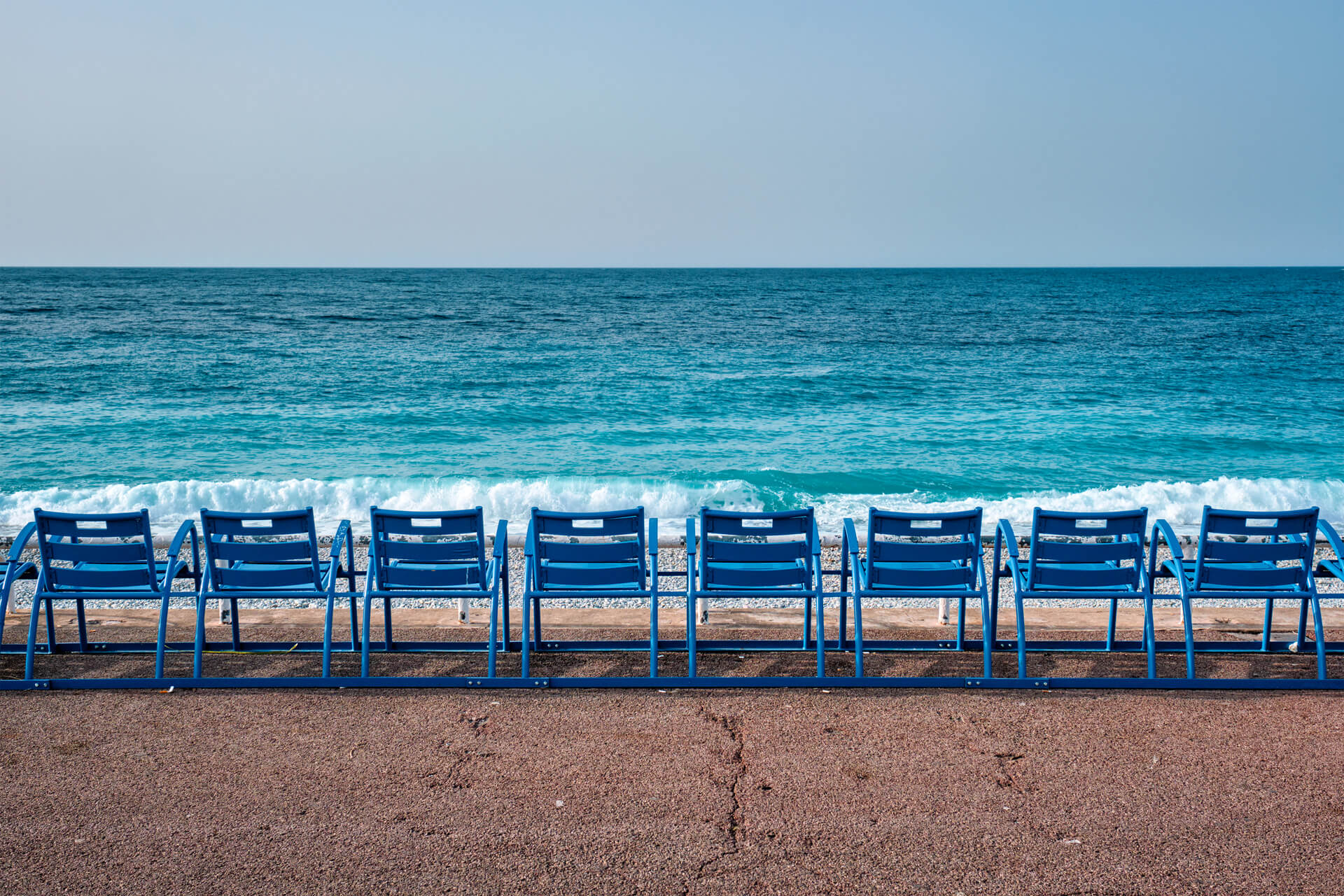 Eine Reihe blauer Stühle direkt am Strand von hinten fotografiert.