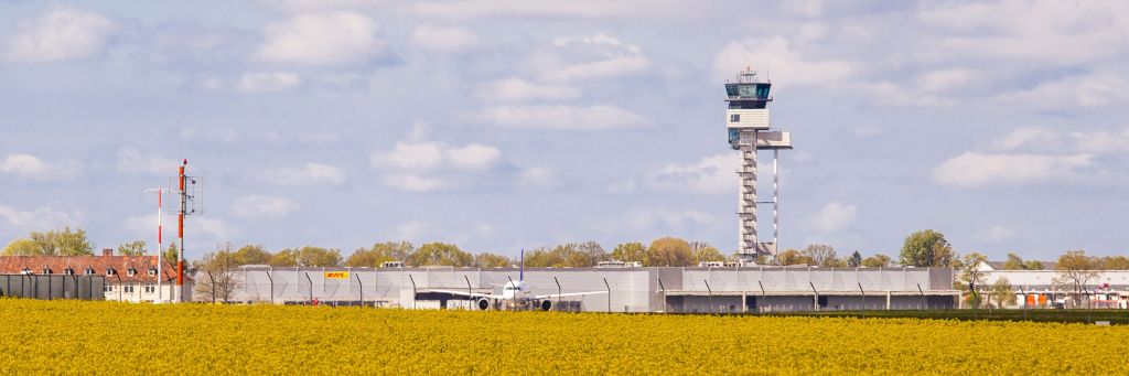 Hinter einem leuchtend gelben Rapsfeld sieht man den Tower vom Flughafen Hannover.