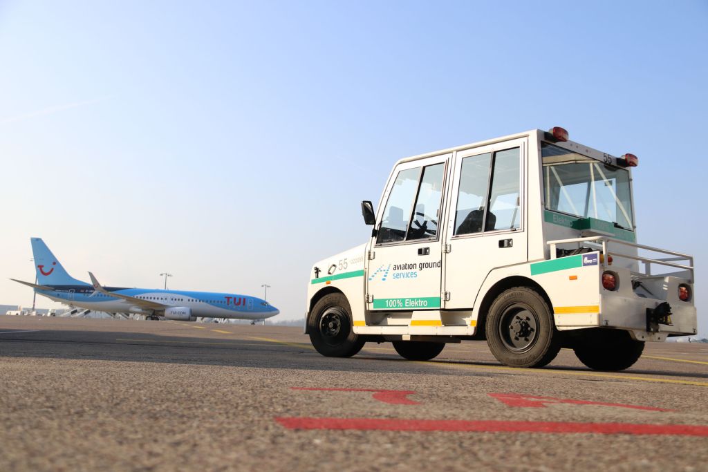 AGS E-Schlepper auf dem Vorfeld, im Hintergrund rollt eine TUIfly Maschine.